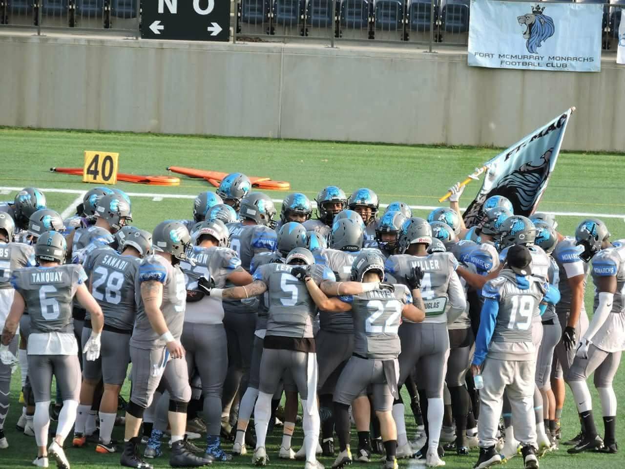 Monarchs team huddle with the team flag raised on the field