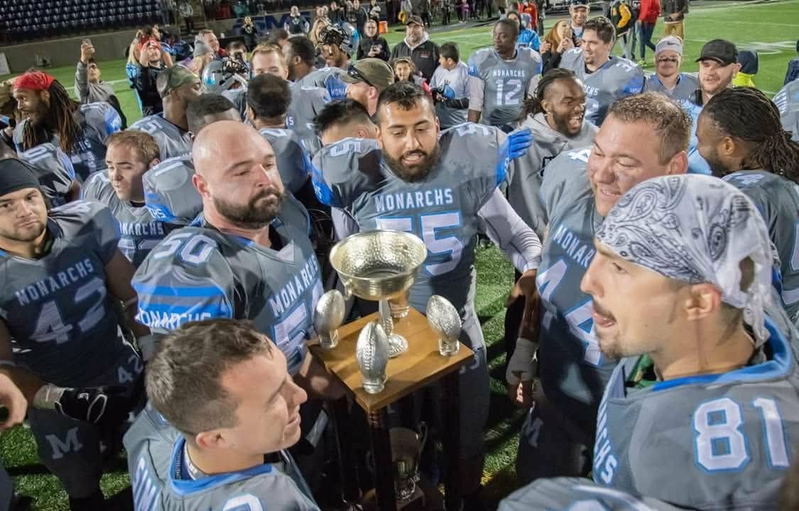 Monarchs players gathered around the championship trophy on the field