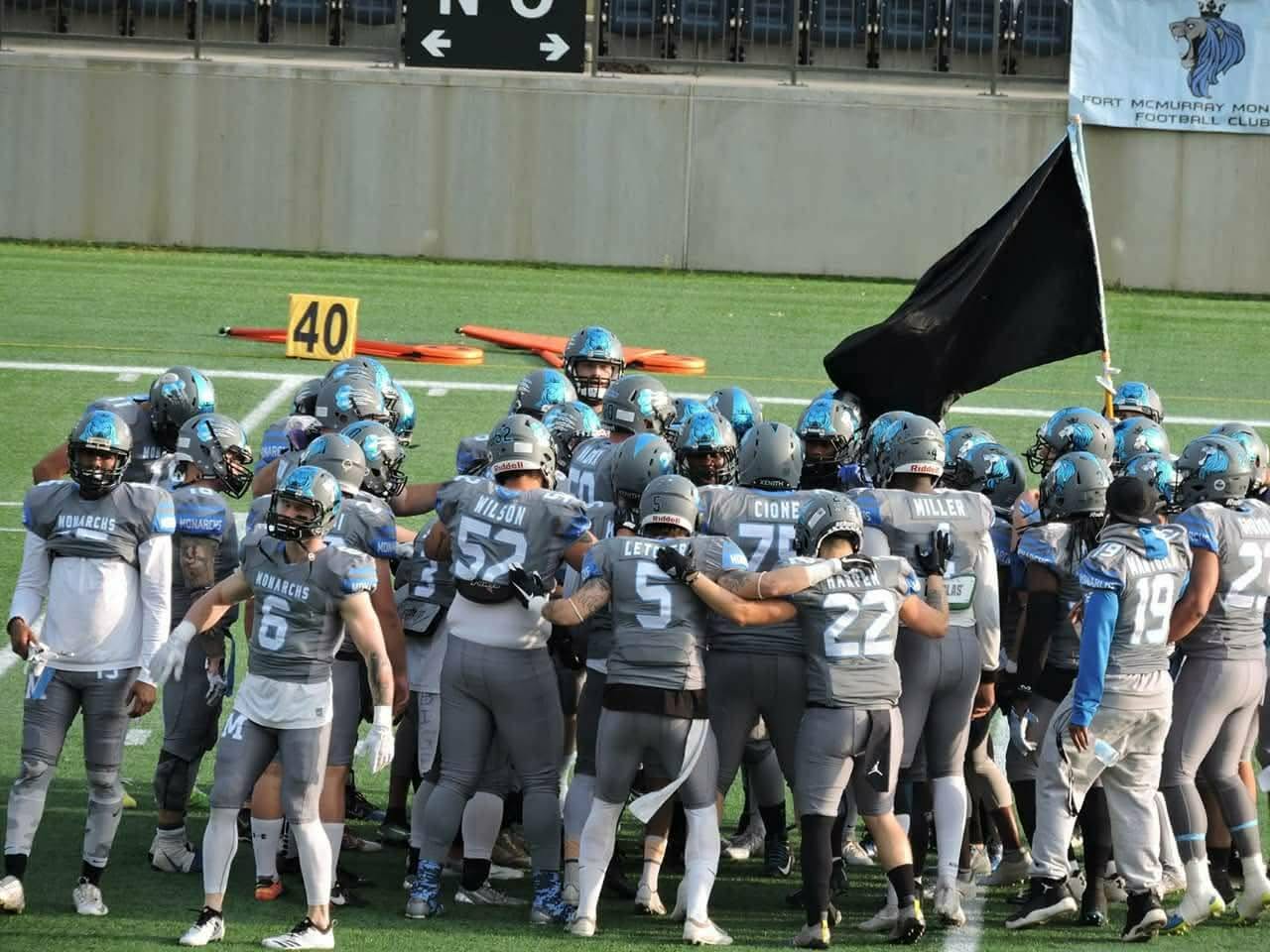 Monarchs team huddle at the 40-yard line with the Monarchs banner