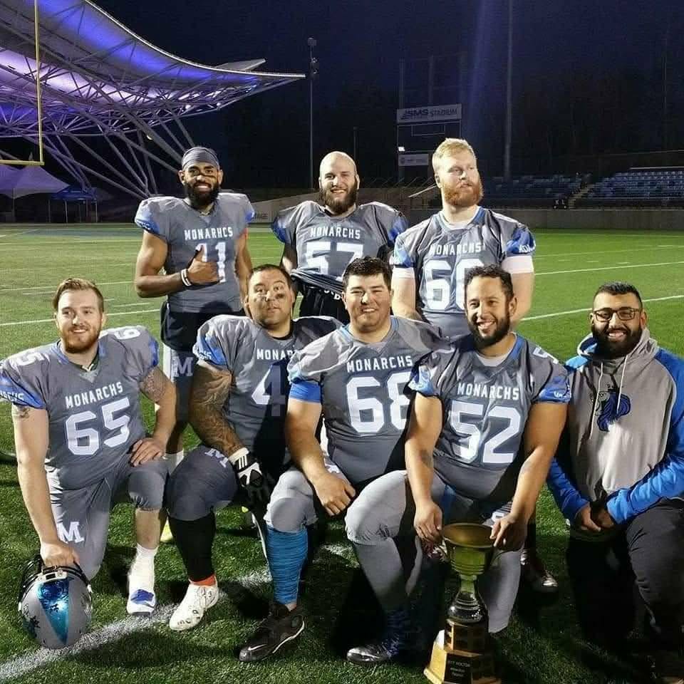 Monarchs offensive linemen posing with championship trophy at SMS Stadium